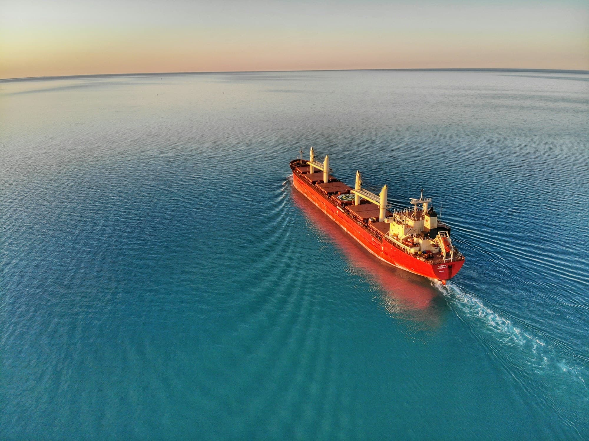 Aerial view of a cargo vessel underway in open water, seen from above with its wake trailing behind.